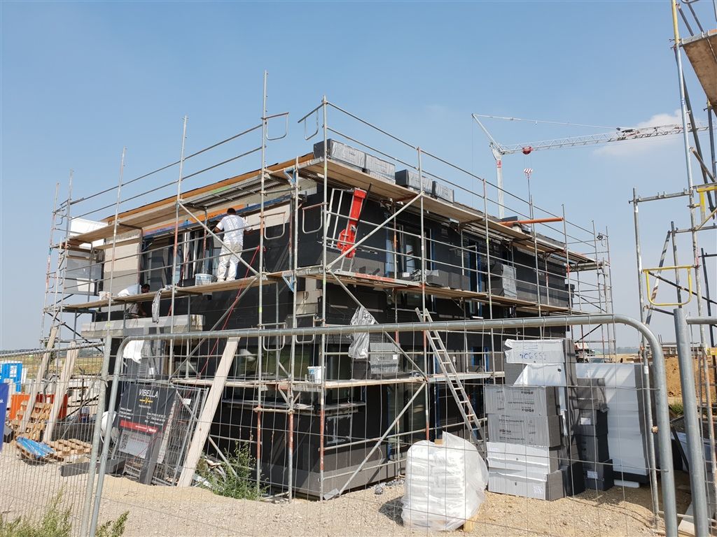 Zweigeschossiger Rohbau mit Gerüst, an der Fassade wird die Dämmebene angebracht, Kran im Hintergrund.