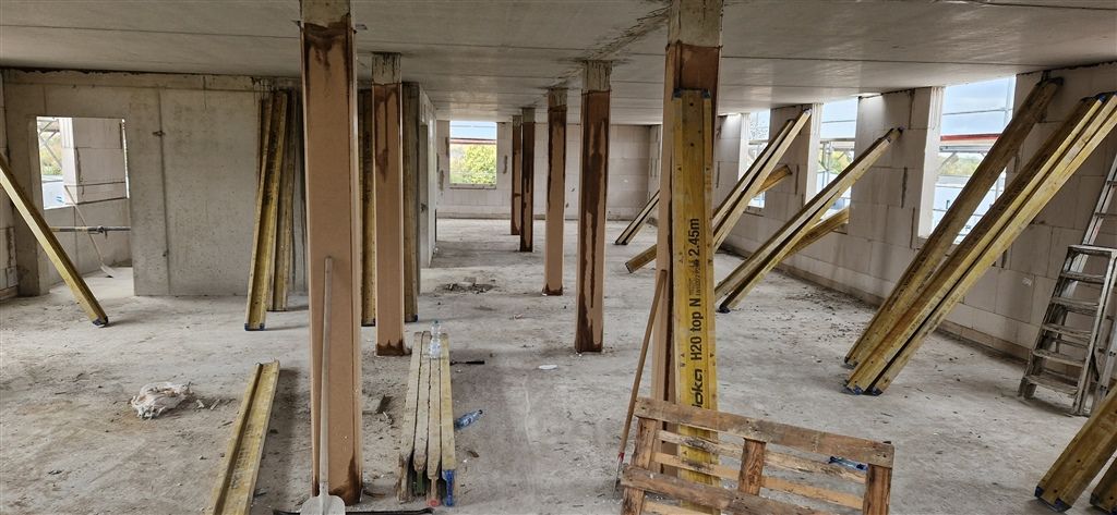 Innenraum eines Rohbaus mit Betonstützen, Deckenrand und gelben Baustützen während einer Begehung.