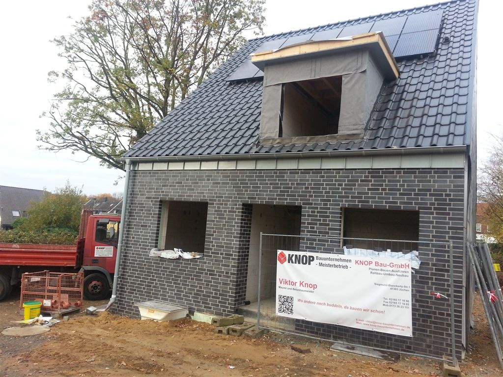Rohbau eines Einfamilienhauses mit dunklem Verblendmauerwerk und ausgesparten Fensteröffnungen.
