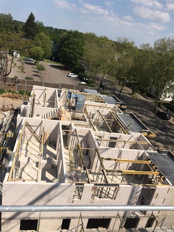 Blick von oben auf ein Geschoss im Rohbau mit tragenden Wänden, Deckenrändern und gelben Abstützungen.